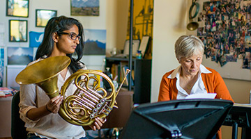 student with her french horn working with a professor